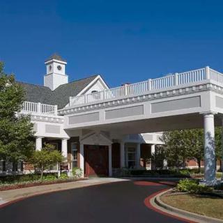 A large building with a covered entrance and columns, featuring a driveway.