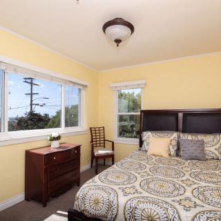A cozy bedroom with a patterned bedspread, wooden furniture, and large windows.