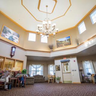 A spacious and inviting lobby featuring a chandelier, comfortable seating, and artwork, illuminated by natural light.