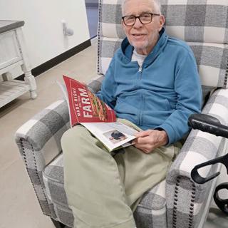 An elderly man sitting in an armchair, reading a book indoors.