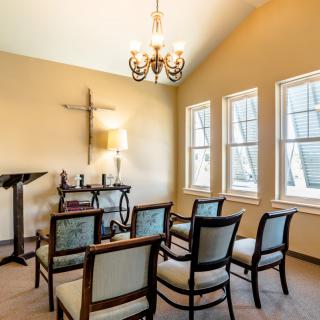 A small chapel interior with chairs arranged in rows, a pulpit, and a cross on the wall.