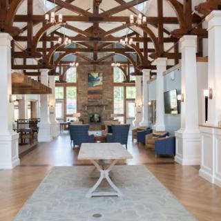 An elegantly designed lobby with high wooden beams, white columns, and a cozy stone fireplace.