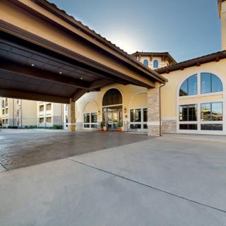 A wide view of a building entrance with large windows and covered driveway.