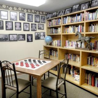 A cozy library room with bookshelves, a checkers board on the table, and framed photos on the wall.