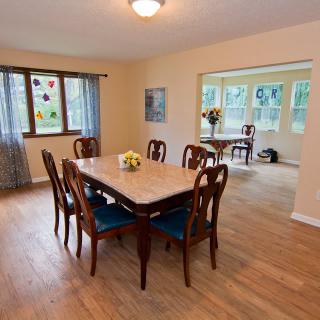 A cozy dining room featuring a large table with chairs, wood flooring, and ample natural light from the surrounding windows.