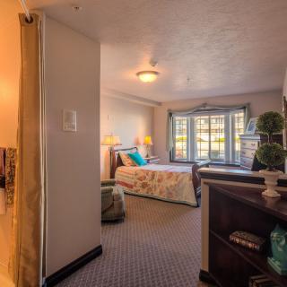 A cozy bedroom with warm lighting, featuring a neatly made bed, decorative pillows, and a large window.