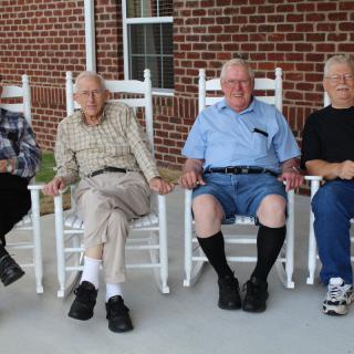 A group of elderly individuals sitting on rocking chairs outside.