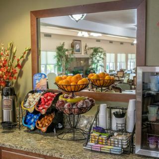 A well-stocked breakfast area with fruit, snacks, and beverages displayed on a counter.