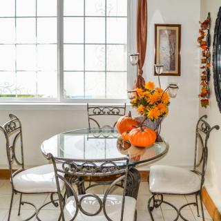 A cozy dining room with a glass table and iron chairs, adorned with pumpkins and fall decorations.