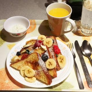 A delicious breakfast featuring French toast with bananas and berries, accompanied by a cup of orange juice and a bowl of yogurt.