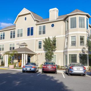 A multi-story residential building with parked cars in front during the daytime.