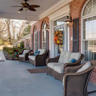 A cozy porch featuring wicker seating with cushions, adorned with fall decorations.