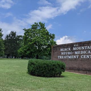 The entrance of the Black Mountain Neuro-Medical Treatment Center, surrounded by green space and trees under a partly cloudy sky.