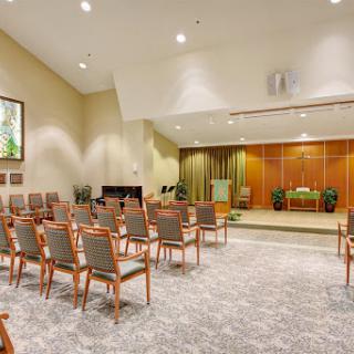 A well-lit interior room set up for a gathering, featuring rows of chairs and a small stage.