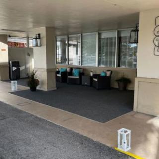 A cozy outdoor seating area near a building entrance, featuring cushioned chairs, lanterns, and decorative plants.