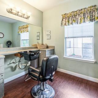 A well-lit salon room featuring a barber chair, mirror, and sink next to a window with floral curtains.