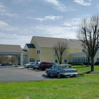 A view of a hotel with a parking lot filled with cars, set against a backdrop of a partly cloudy sky.