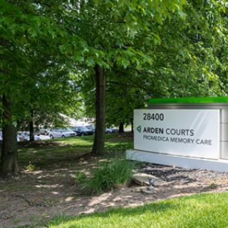 A sign for Arden Courts Memory Care facility surrounded by trees.