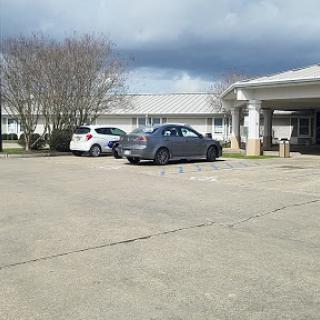 A view of a parking lot with two cars parked, surrounded by buildings and trees under a cloudy sky.