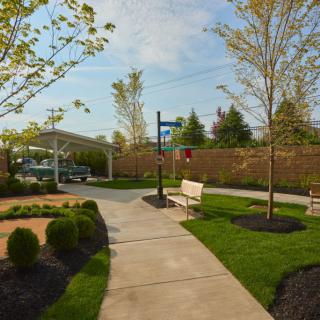 A serene park pathway with a bench, surrounded by neatly landscaped greenery and trees.
