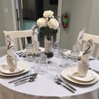A beautifully set dining table with an elegant white theme, featuring folded napkins, glasses, and a central flower arrangement.