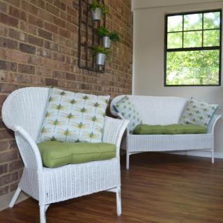 A cozy indoor seating area with wicker chairs and green cushions against a brick wall.