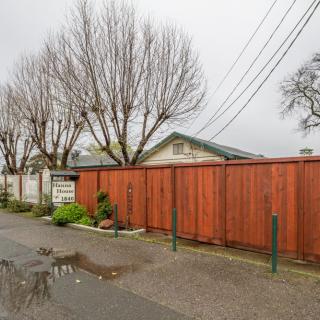 A residential street with a wooden fence, bare trees, and overcast skies.