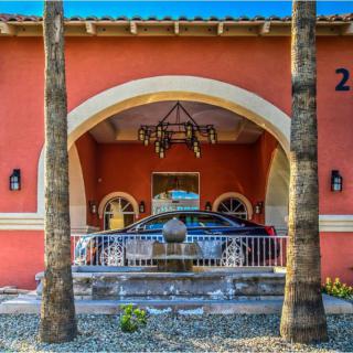 A car parked under an archway at the entrance of a building, surrounded by palm trees.