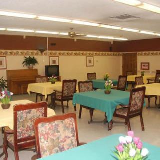 A spacious dining room with multiple tables and chairs, decorated with flowers.