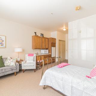 A cozy studio apartment featuring a bed, seating area, and kitchenette.