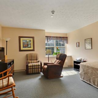 A cozy bedroom with a bed, chairs, and a window allowing natural light.