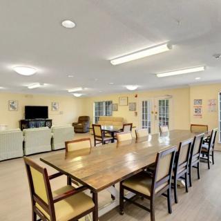 A spacious common room with a large dining table, chairs, and a seating area with couches and a television.