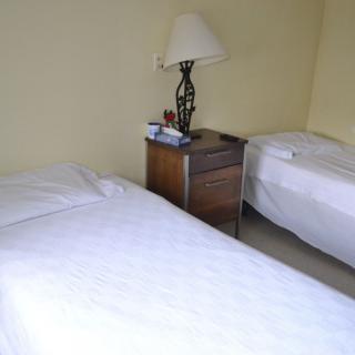 A minimalist bedroom with two single beds and a nightstand with a lamp.