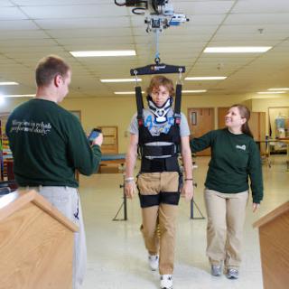 A patient aided by an exoskeleton during rehabilitation, guided by healthcare professionals.