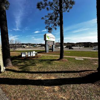 A view of a business sign surrounded by trees and open grass under a clear blue sky.