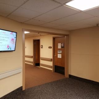 A view of a healthcare facility's hallway, featuring doors and a digital display.
