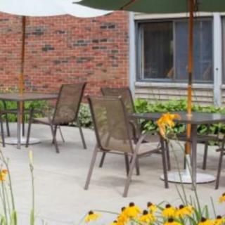 A cozy patio area with tables, chairs, and an umbrella surrounded by blooming flowers and a brick wall.