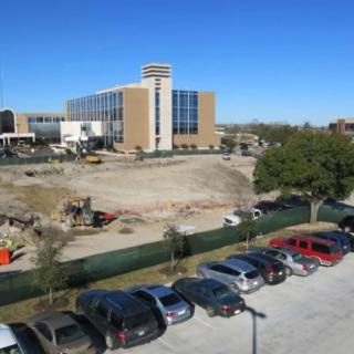 A construction site next to a building with parked cars under a clear blue sky.