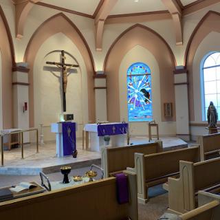 An interior view of a serene church featuring an altar, cross, and stained glass windows.