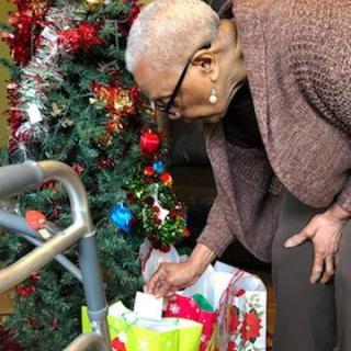 An elderly person looking at Christmas gifts under a decorated tree.