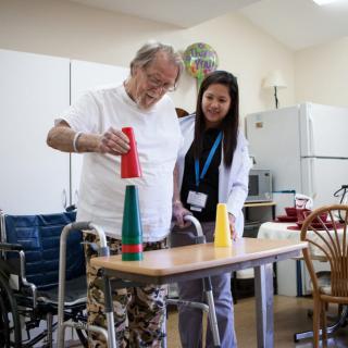 An elderly man receiving physical therapy assistance, stacking cups with guidance from a healthcare provider.