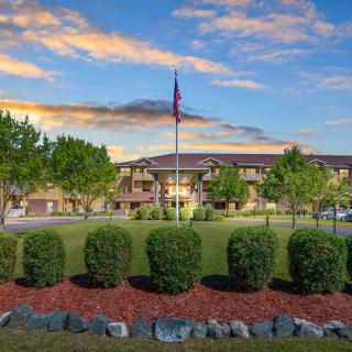 A scenic view of a building with a flagpole, surrounded by landscaped greenery and set against a backdrop of colorful clouds at sunset.