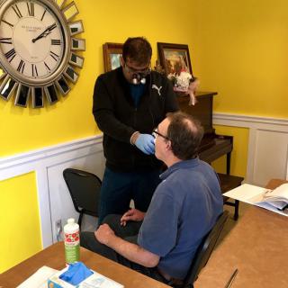 A healthcare professional examines a patient in a clinic room with a yellow wall.