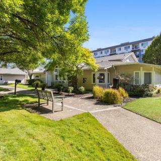 A well-maintained garden area with a pathway and benches in front of a residential building on a sunny day.