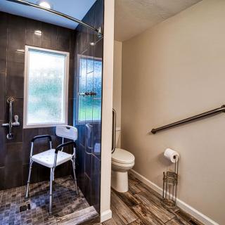 A modern bathroom featuring an accessible shower with a chair and a toilet equipped with a grab bar.