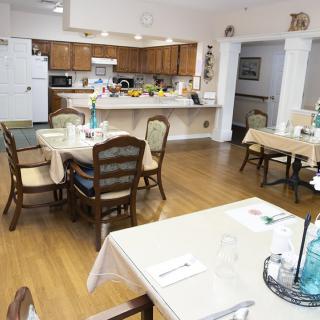 A cozy dining area with a connected kitchen, featuring tables and chairs set for dining.