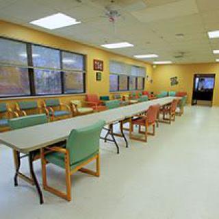 A spacious dining area with long tables and a variety of chairs, illuminated by bright overhead lights.