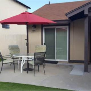 A backyard patio with a red umbrella, table, and chairs next to a house.