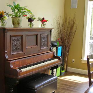 A beautifully arranged corner with a vintage piano and decorative plants, bathed in natural light.