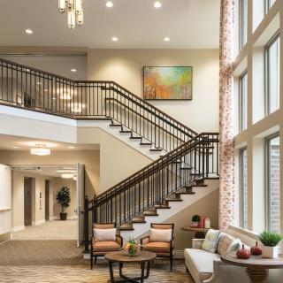 A modern lobby featuring a grand staircase with elegant lighting, comfortable seating, and large windows.